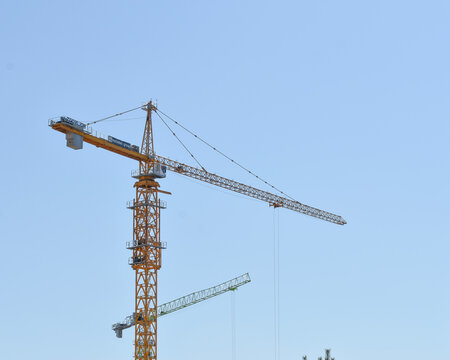 Tall yellow construction tower crane working against a clear blue sky background during an urban building project day