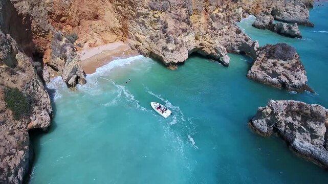 Dramatic aerial perspective of a tourist boat cruising through turquoise waters near a secluded sandy beach and impressive rock formations at praia do alemao in portimao, algarve, portugal