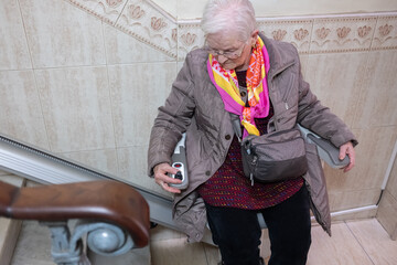 Senior woman with disability operating a medical chair stairlift, gaining mobility and independence at home © D.Petrus