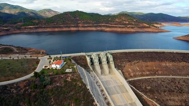 Aerial perspective of the odelouca dam and its reservoir, showing the concrete spillway and surrounding mountainous landscape in the algarve region of southern portugal on a cloudy day
