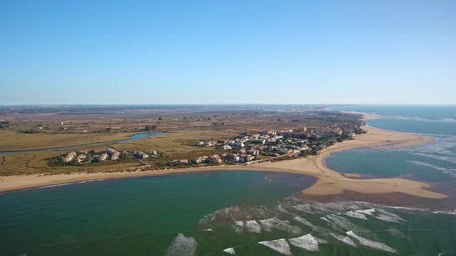 Scenic aerial footage showing the beautiful coastline of playa isla canela in ayamonte, spain, with gentle waves from the atlantic ocean meeting the sandy shore and a clear blue sky above