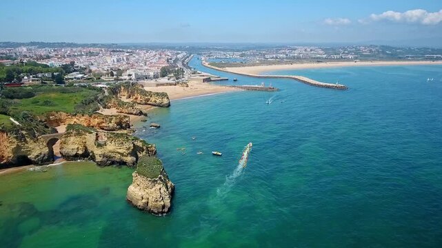 Stunning aerial view of a speedboat navigating the turquoise ocean waters near the picturesque ponta da piedade and camilo beach, with the city of lagos, portugal visible in the background
