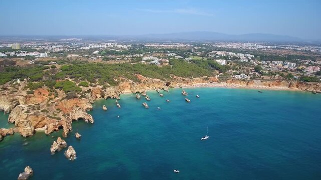 Stunning aerial perspective showing the beautiful algarve coastline, featuring dramatic cliffs, turquoise water, sandy beaches, and the city of portimao in the background on a sunny day