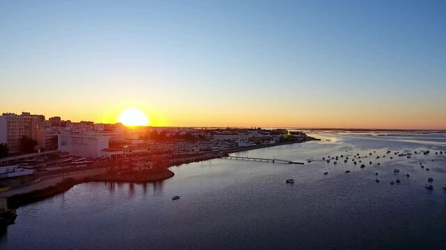 Breathtaking aerial view showing a vibrant sun rising over a picturesque european coastal town, with calm harbor waters reflecting the morning light and boats peacefully floating near the shoreline