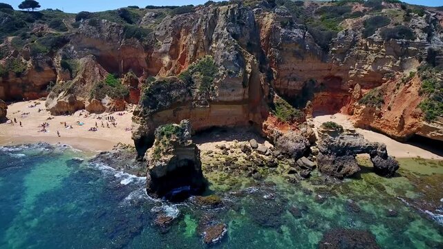 Stunning aerial footage revealing the picturesque camilo beach in the algarve region of portugal, showcasing its golden sands, towering cliffs, and turquoise waters with tourists sunbathing