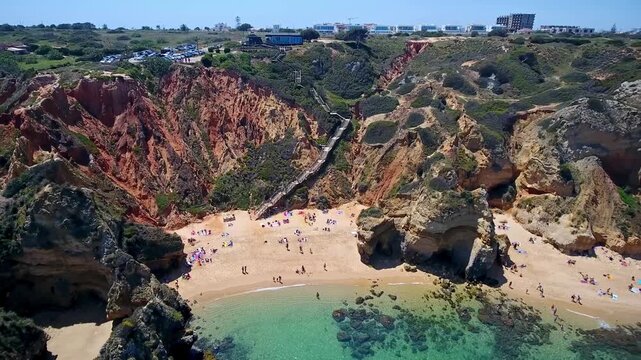 Aerial view retreating from camilo beach, revealing turquoise atlantic waters, sandy shore and dramatic algarve cliffs at ponta da piedade with tourists enjoying a sunny summer day