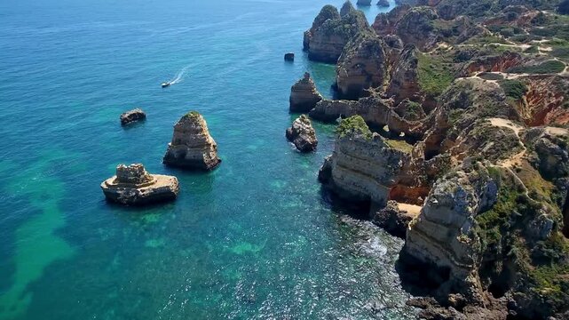 Sunny aerial view of the beautiful ponta da piedade coast, with its impressive rock formations, cliffs, turquoise waters, and a boat navigating the atlantic ocean near lagos, portugal