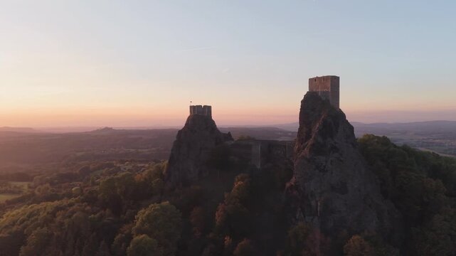 Aerial view of Trosky Castle at sunset with historic ruins on rocky peaks surrounded by forest during golden hour in Troskovice, Liberec Region, Czechia.