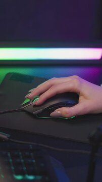 Woman hand with manicured nails operates gaming mouse on desk illuminated by colorful LED lighting. focus remains consistently on interaction between fingers and device throughout sequence
