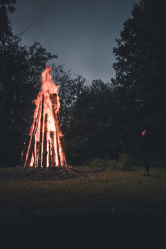 View of a person standing before a large traditional bonfire at night in a forest setting in Laane County, Estonia.
