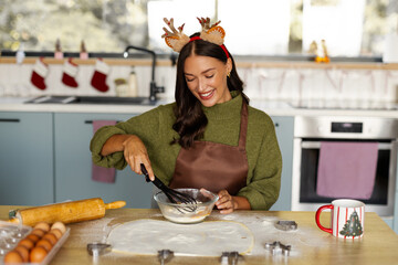 Happy woman wearing reindeer antlers whisking ingredients while preparing homemade Christmas cookies © Home-stock
