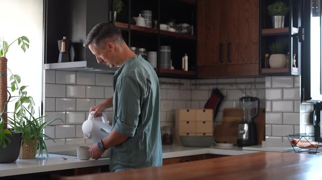 Mature man brewing coffee and stretching his tired neck in the kitchen