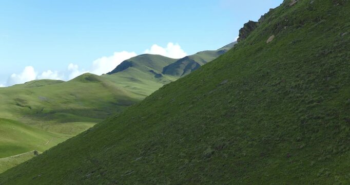 Badimalika region, Bajura, Nepal, drone reveals vast green alpine hills and mountain peaks in Triveni Patan grassland past a steep grassy ridge underneath clear skies.