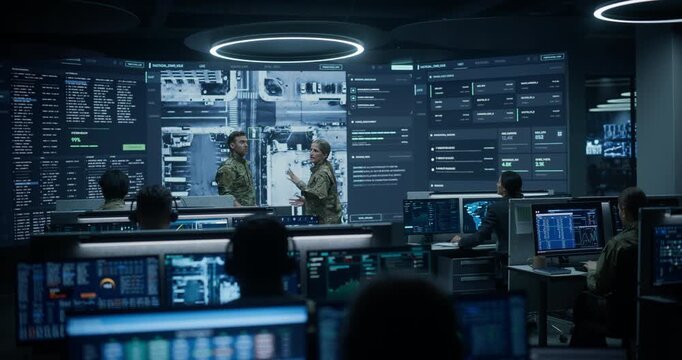 Army Military Surveillance Monitoring Control Room: Two Officers in Uniform Have a Meeting and Talk About Drone Reconnaissance Footage on Screen While Specialists Run AI Big Data Analysis for Defense