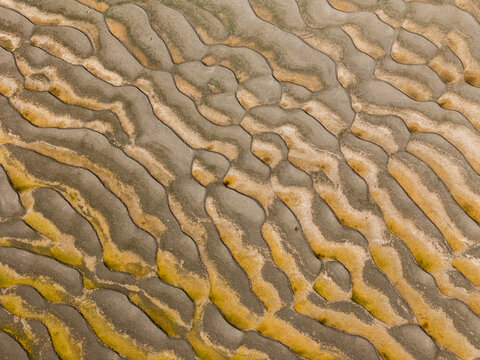 An overhead perspective capturing the intricate patterns and textures formed by water currents on a sandy shoreline during a receding tide