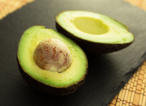 ripe halved avocado with bone on black stone board