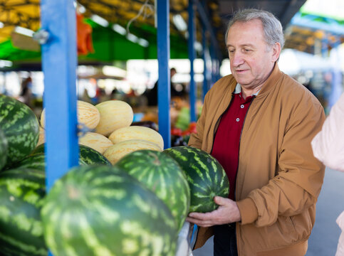 elderly man and woman are buying a watermelon at an open-air market