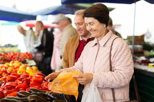 elderly man and woman are buying peppers at an open-air market