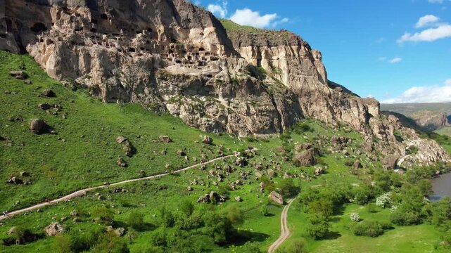Aerial view moving alongside the ancient cave city of vardzia, a historic monastery complex carved into the erusheti mountain, showcasing its many levels and dwellings under a blue sky