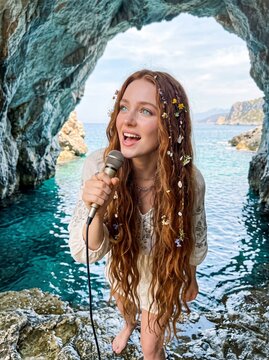 Giovane donna cantante che si esibisce con un microfono durante un concerto dal vivo in un contesto naturale suggestivo