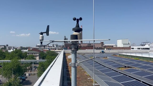 Rooftop weather station with anemometer beside solar panels overlooking an urban neighborhood under a clear blue sky on a sunny day