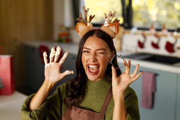 Playful woman in reindeer antlers showing her flour-covered hand and cookie cutter © Home-stock