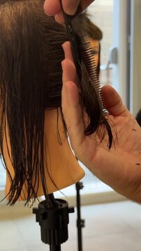 Vertical video featuring a close-up of a professional hairstylist's hands precisely cutting and styling hair in a modern beauty salon