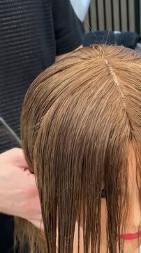 Vertical video featuring a close-up of a professional hairstylist's hands precisely cutting and styling hair in a modern beauty salon