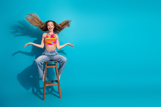 Vibrant young woman posing on a stool with lively energy and cheerful expression, showcasing fun