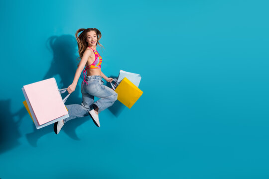 Cheerful young woman jumping with colorful shopping bags against a vibrant blue background expressing happiness and joy