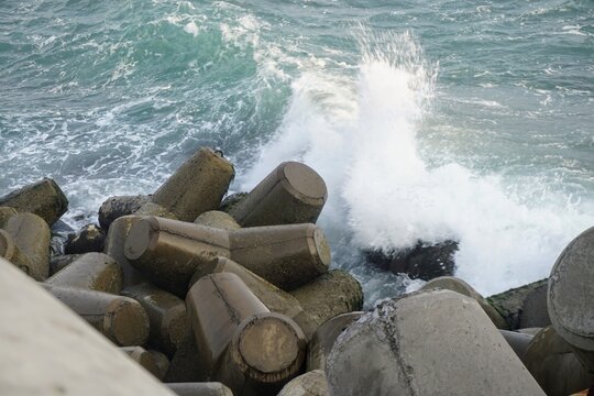 Ocean wave splash crashing against concrete tetrapod breakwater structures along the coastline.