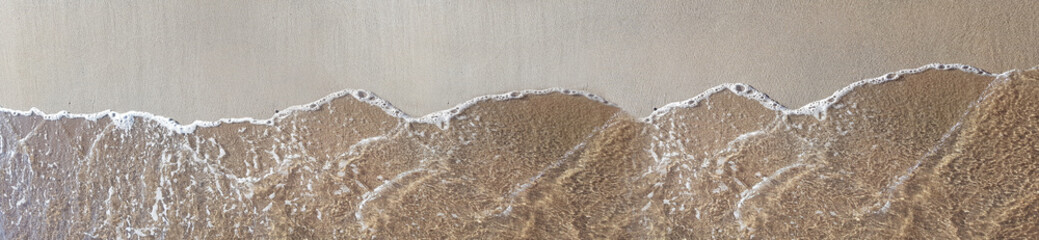 Aerial view of clear ocean water waves washing over wet sandy beach shore in soft sunlight © MonTeArt