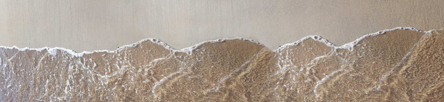 Aerial view of clear ocean water waves washing over wet sandy beach shore in soft sunlight