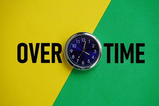 OVERTIME. Work-related concept. Working beyond scheduled hours, with additional pay for the extra time. Clock background centered behind the word