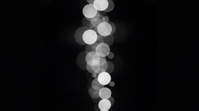 Vertical trail of soft glowing white bokeh circles isolated on black background