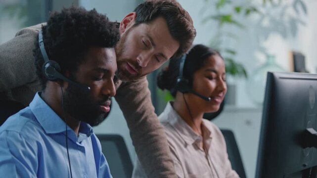 Caucasian business boss man coming checking helping teaching African American intern with online computer task to multiethnic hotline operators working in call center office callcenter leadership help