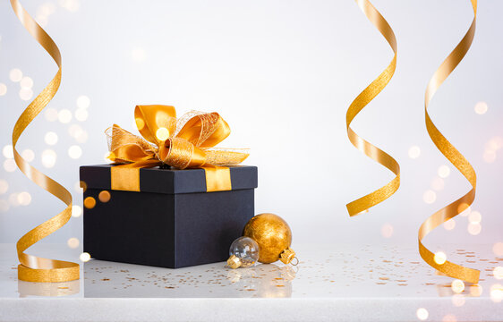 Black gift box with gold beautiful bow and abstract curling ribbons on white table