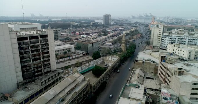 Aerial view of the dense urban landscape of Karachi with historic buildings, busy streets, and the distant port area under a hazy sky in Karachi, Sindh, Pakistan.