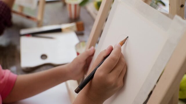 Caucasian girl sketching outline on canvas with pencil during art masterclass. Visual is ideal for promoting creative education and children development programs