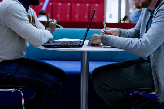 Two men, one Black and one white, work together at a cafe table with laptop
