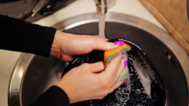 Slow motion shows woman with colorful manicure washing soapy bowl, kitchen sink