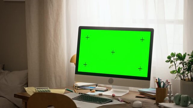 Desktop computer displaying green screen with tracking marks standing on study table. Suitable for showcasing online learning interface, e-learning platform, or educational app mockup