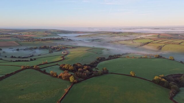 Aerial view of the misty rural countryside landscape at sunrise with green fields and hedgerows in Looe, England, United Kingdom.