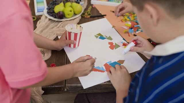 Caucasian kids gluing colorful paper collage during art masterclass, top view. Footage suitable for creative education marketing, workshop promotions, and school campaigns