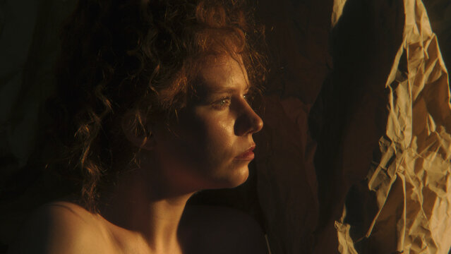 Close Up of Curly Redhaired Woman Looking Through Narrow Space of Warm Sunlight, Symbolizing Self Exploration, Identity and Awareness. Atmospheric Creative Concept About Discovering Inner Self.