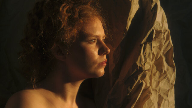Woman Surrounded by Crumpled Paper Pauses in Private Inner World, Reflecting on Thoughts and Emotions. Warm Cinematic Light and Deep Shadows Create an Intimate Visual Metaphor For Self Discovery.