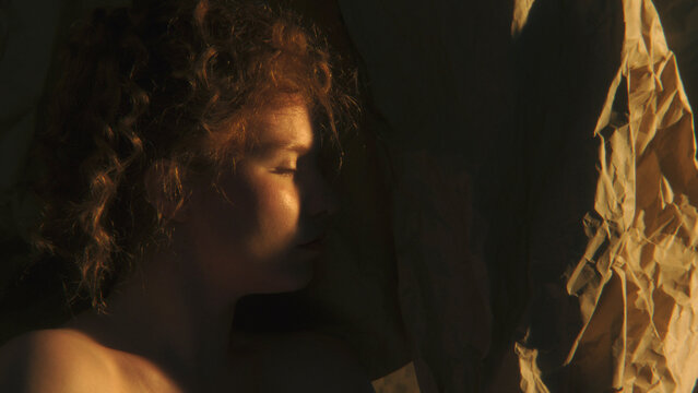 Close Up of Curly Redhaired Woman Looking Through Narrow Space of Warm Sunlight, Symbolizing Self Exploration, Identity and Awareness. Atmospheric Creative Concept About Discovering Inner Self.