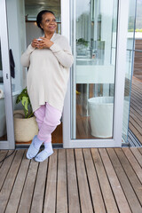 Senior African American woman standing at home doorway holding mug, wearing cardigan, copy space © WavebreakMediaMicro