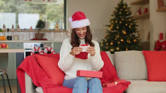 Excited woman opening wrapped Christmas present and finding red Christmas stockings inside, holding them up and smiling with delight at home, 4K
