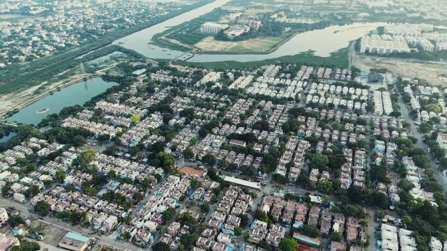 Aerial view of symmetrical residential community buildings surrounded by lush greenery, urban streets, and nearby water bodies in India.